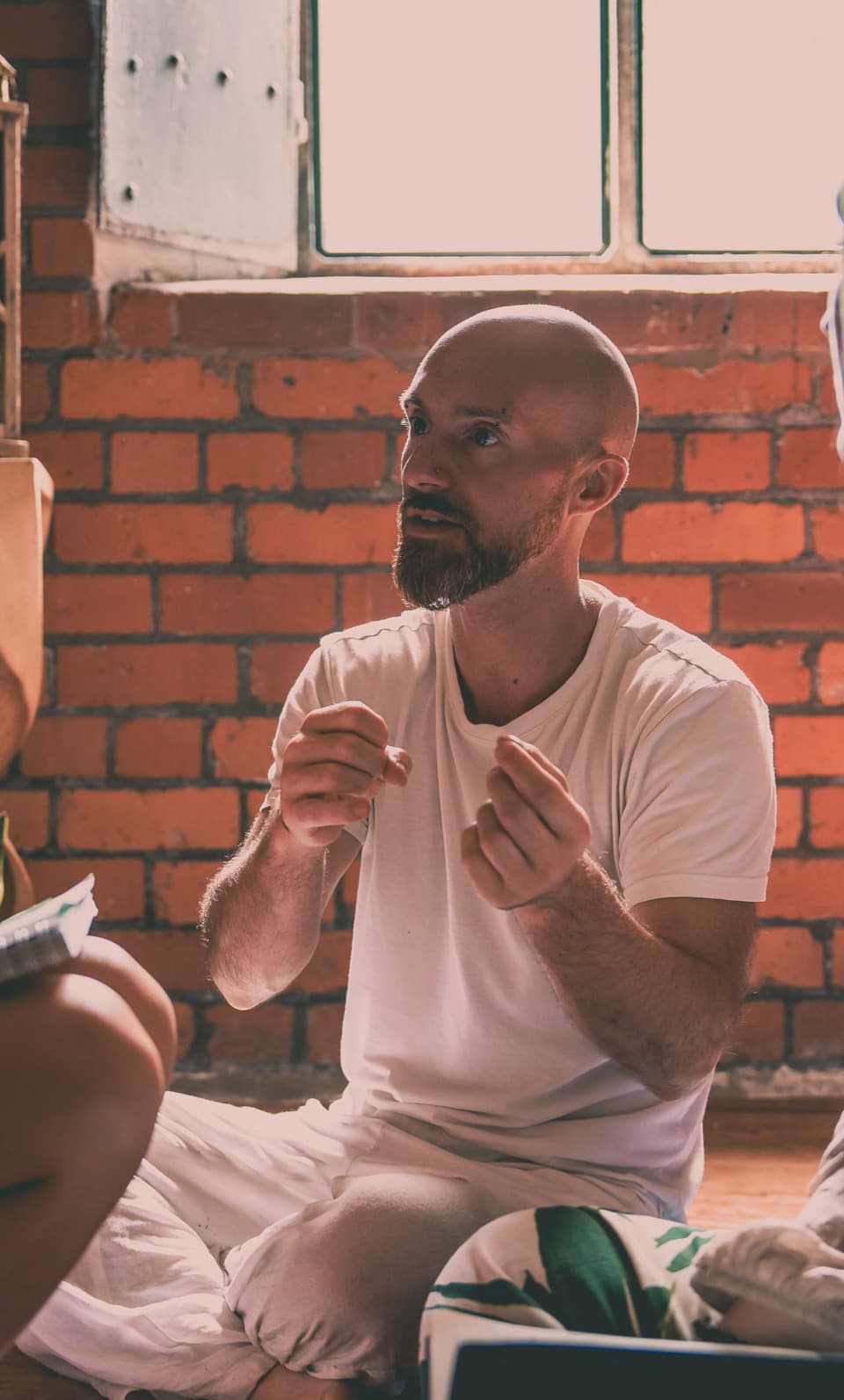 Ben North speaking during a training, seated against a brick wall.